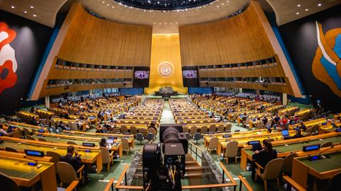 Der an ein Amphitheater erinnernde Innenraum der Vereinten Nationen während einer Sitzung. Die Reihen sind unregelmäßig besetzt.