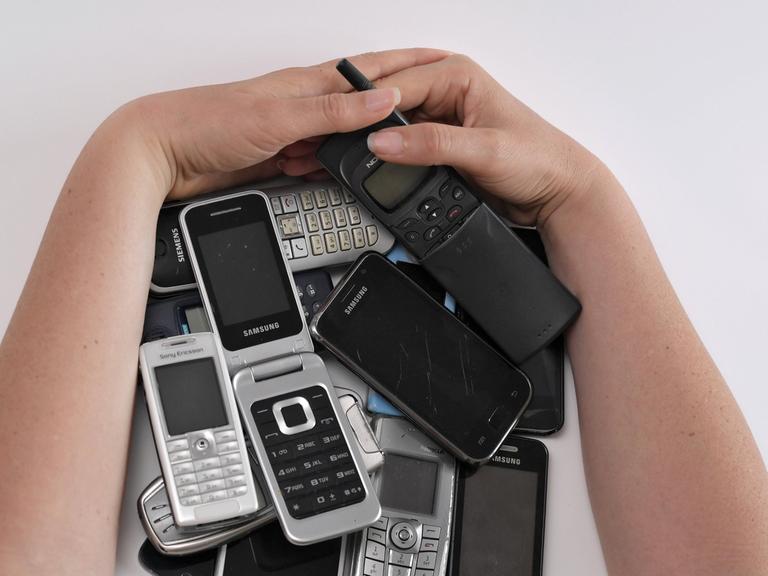 Eine Frau hält eine große Zahl an alten Handys zwischen ihren Armen.
