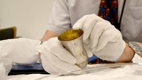 Matthias Weniger, Leiter der Provenienzforschung des Bayerischen Nationalmuseums, zeigt einen in der NS-Zeit geraubten Silberbecher - man sieht nur seine behandschuhten Hände, die den Becher halten