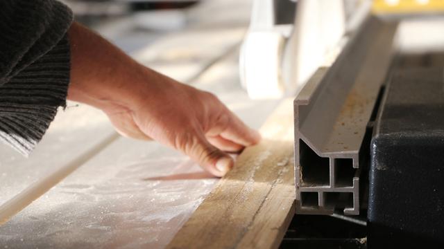 Arbeit in einer Schreinerwerkstatt - Eine Hand führt ein Holzstück an einem Sägetisch.