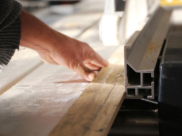Arbeit in einer Schreinerwerkstatt - Eine Hand führt ein Holzstück an einem Sägetisch.
