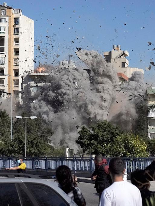 In Beirut sehen Menschen dabei zu, wie ein von einem israelischen Angriff bombardiertes Haus in sich zusammenfällt. 