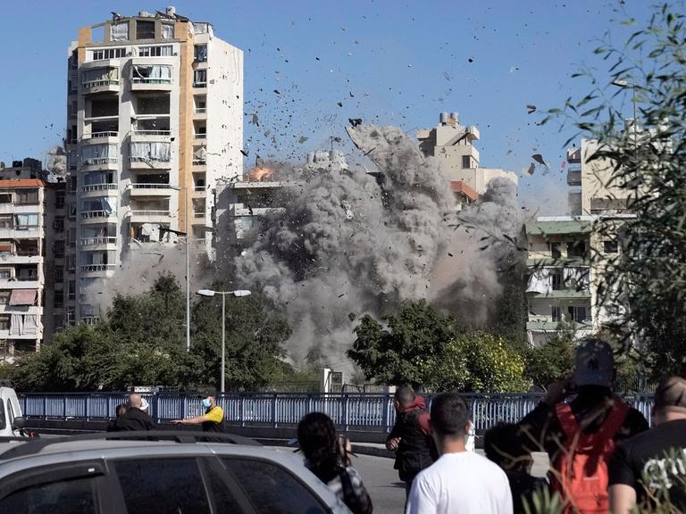 In Beirut sehen Menschen dabei zu, wie ein von einem israelischen Angriff bombardiertes Haus in sich zusammenfällt. 