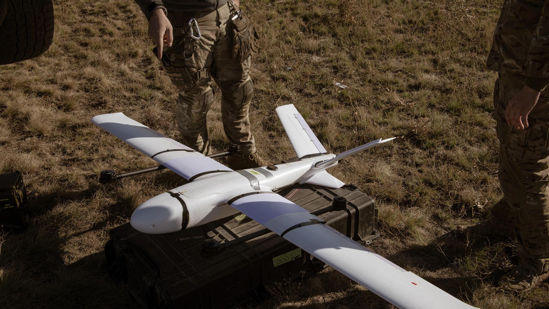 Zwei Soldaten stehen neben dem Protoypen einer Drohne, die auf dem Boden zum Einsatz bereit liegt.