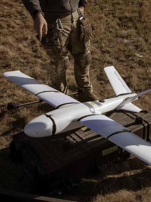 Zwei Soldaten stehen neben dem Protoypen einer Drohne, die auf dem Boden zum Einsatz bereit liegt.