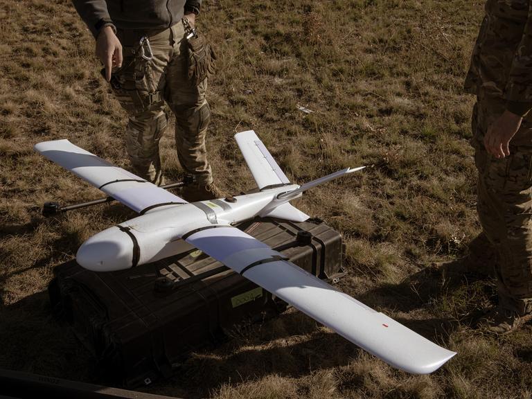 Zwei Soldaten stehen neben dem Protoypen einer Drohne, die auf dem Boden zum Einsatz bereit liegt.