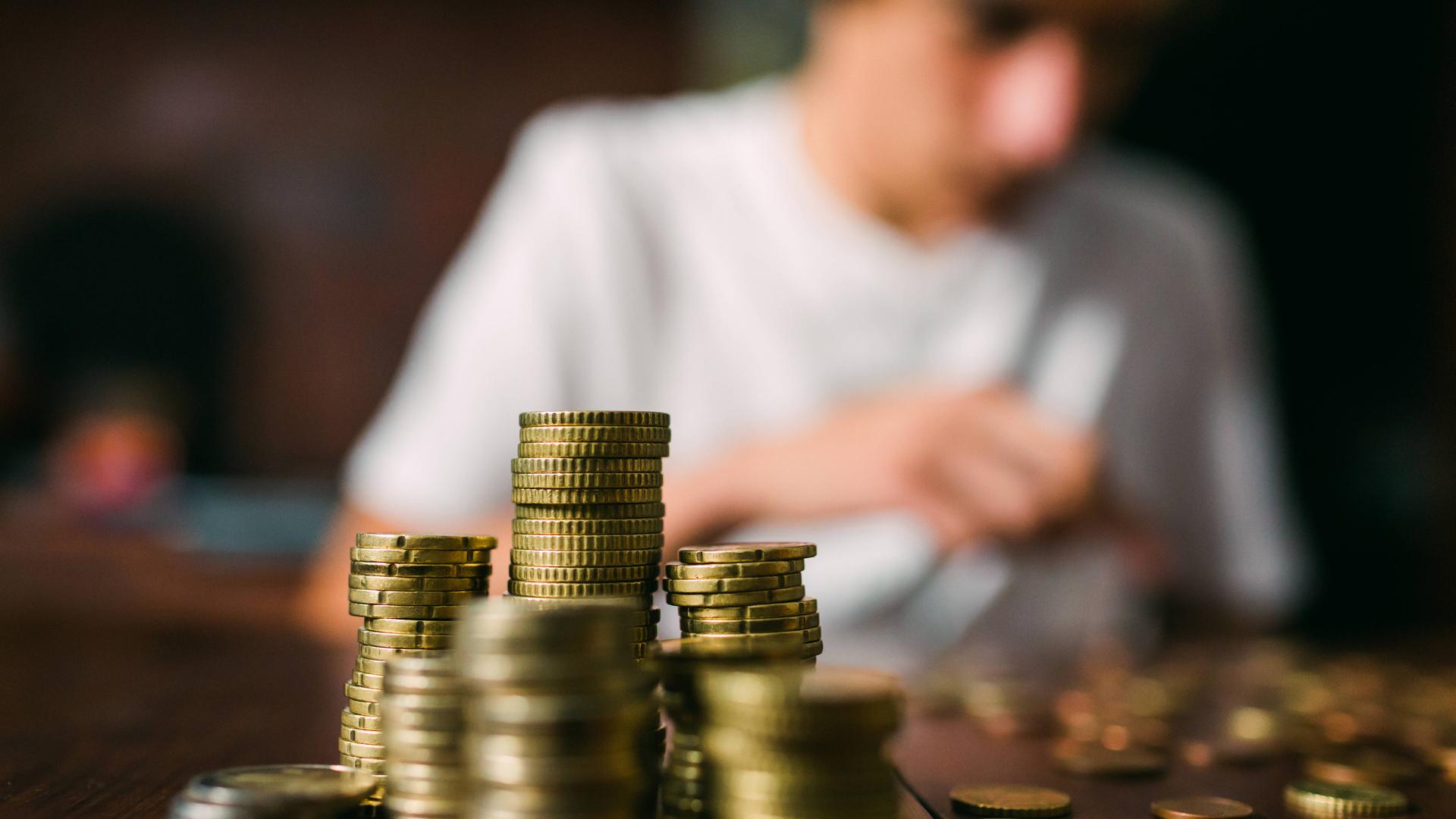 Ein Jugendlicher sitzt an einem Schreibtisch und zählt Geldmünzen.