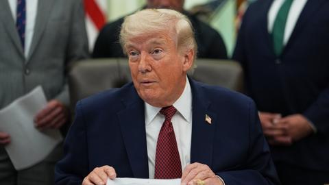 US-Präsident Donald Trump spricht im Oval Office des Weißen Hauses. Im Hintergrund stehen Männer in Anzügen. 