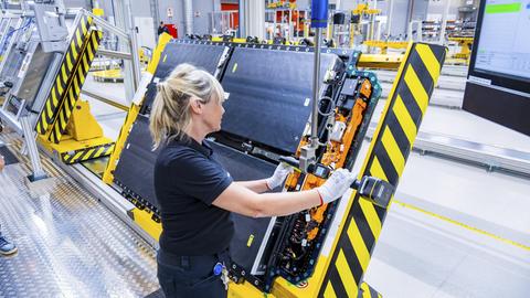 Eine Frau steht in einer Fertigungshalle und stellt Antriebsbatterien für ein vollelektrisches Mercedes-Benz-Modell her. Eine Frau steht in einer Fertigungshalle und stellt Antriebsbatterien für ein vollelektrisches Mercedes-Benz-Modell her.
