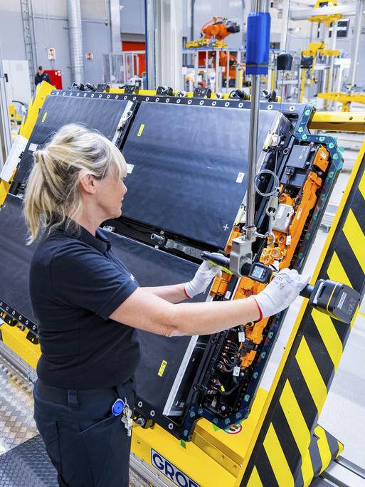 Eine Frau steht in einer Fertigungshalle und stellt Antriebsbatterien für ein vollelektrisches Mercedes-Benz-Modell her.