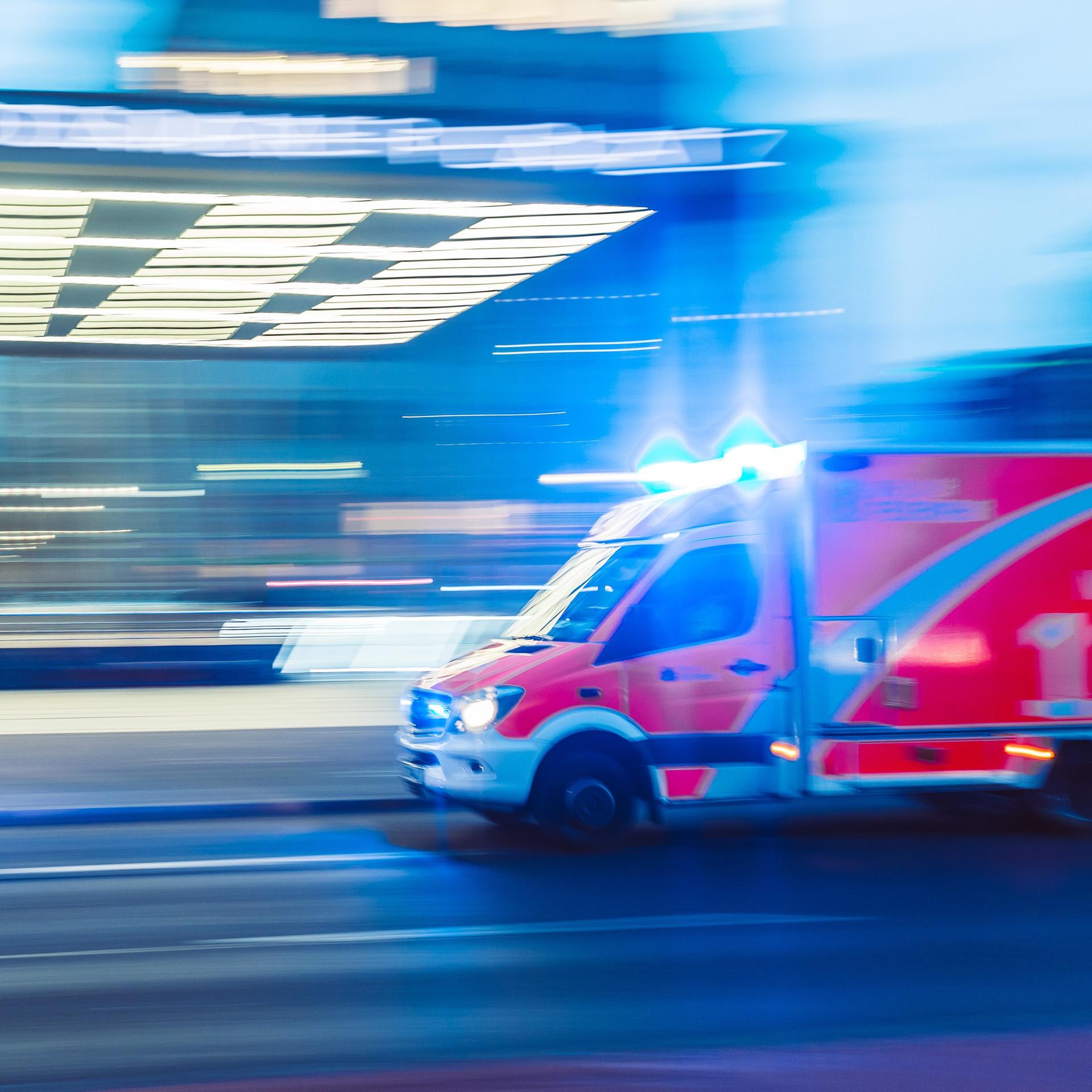 Ein unscharfer weil schnell fahrender Notarztwagen vor einem Gebäude was ebenfalls in der Unschärfe verzerrt wird