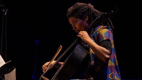 Auf dem Bild sehen wir die Cellistin Tomeka Reid im Profil an ihrem Cello. 