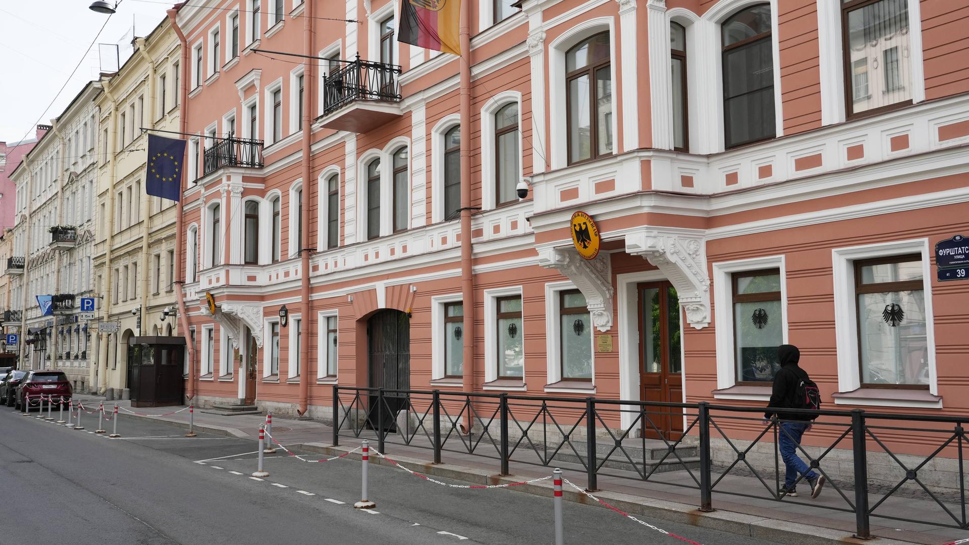 Das Bild zeigt ein Gebäude in St. Petersburg mit einer rot-weißen Fassade. Über der Tür hängen eine deutsche Fahne und ein deutsche Wappen. Das Bild zeigt ein Gebäude in St. Petersburg mit einer rot-weißen Fassade. Über der Tür hängen eine deutsche Fahne und ein deutsche Wappen.