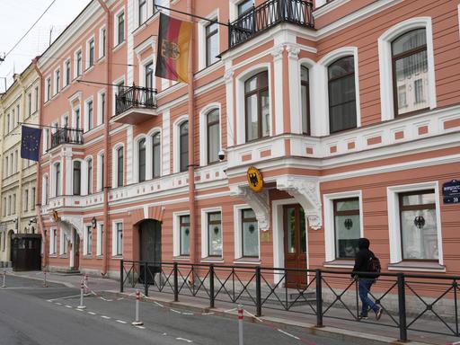 Das Bild zeigt ein Gebäude in St. Petersburg mit einer rot-weißen Fassade. Über der Tür hängen eine deutsche Fahne und ein deutsche Wappen.