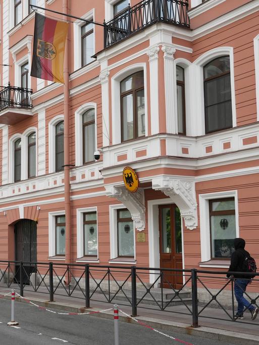 Das Bild zeigt ein Gebäude in St. Petersburg mit einer rot-weißen Fassade. Über der Tür hängen eine deutsche Fahne und ein deutsche Wappen.