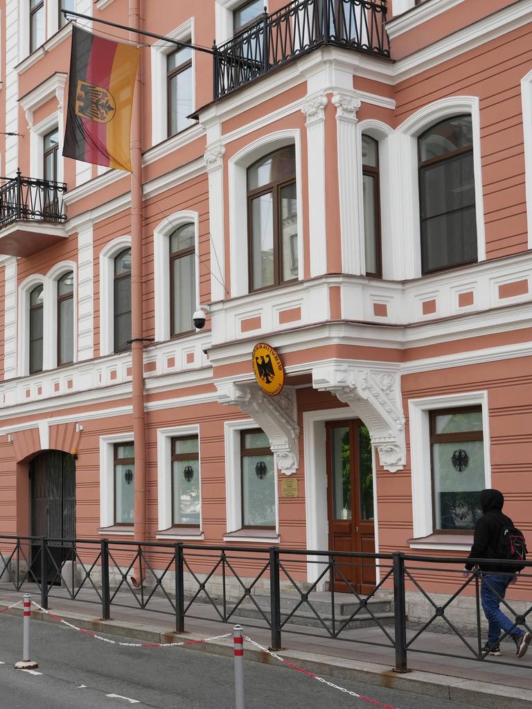 Das Bild zeigt ein Gebäude in St. Petersburg mit einer rot-weißen Fassade. Über der Tür hängen eine deutsche Fahne und ein deutsche Wappen.
