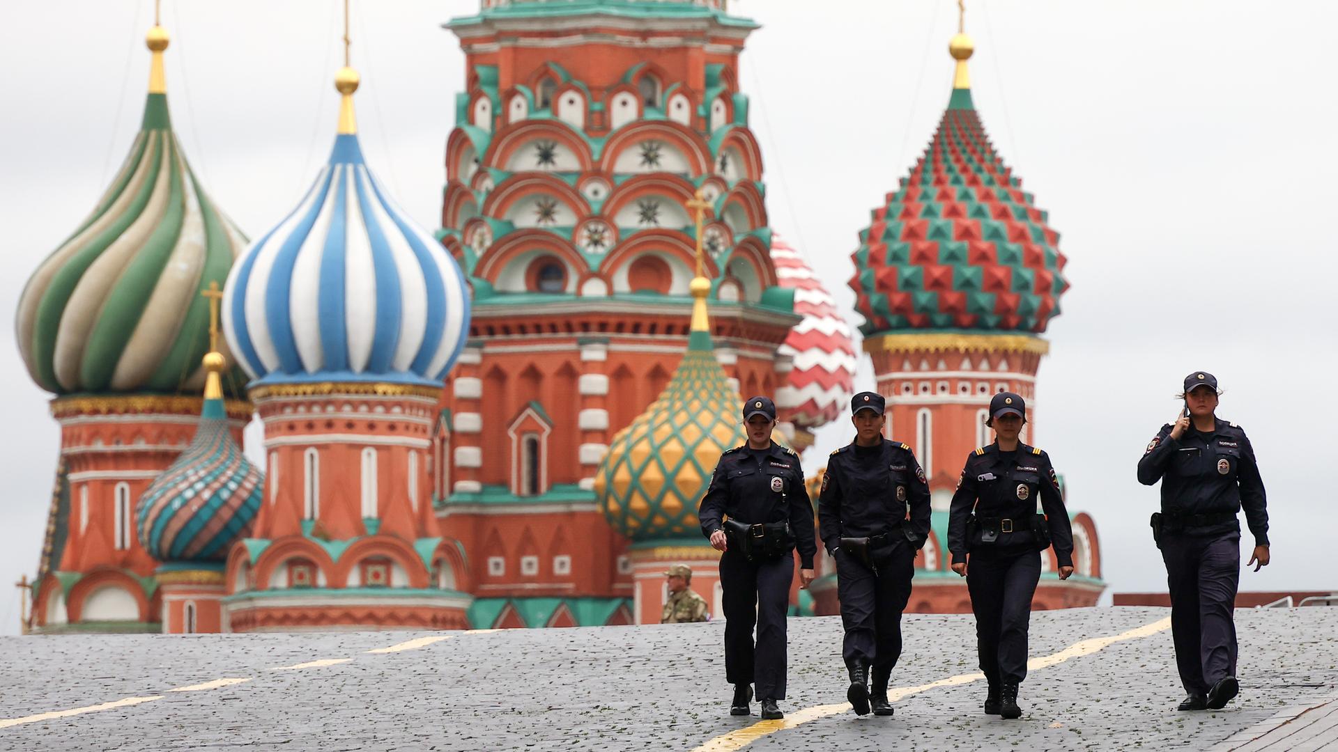 Vier Sicherheitskräfte patrouillieren auf dem Roten Platz in Moskau, im Hintergrund ist die Kathedrale mit bunten Zwiebeltürmchen zu sehen