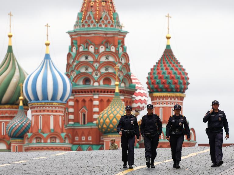 Vier Sicherheitskräfte patrouillieren auf dem Roten Platz in Moskau, im Hintergrund ist die Kathedrale mit bunten Zwiebeltürmchen zu sehen
