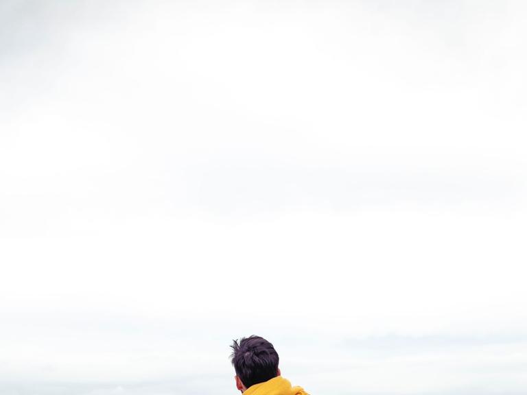 Ein Mensch sitzt am Meer und hat die Arme geöffnet. Ein Mensch sitzt am Meer und hat die Arme geöffnet.