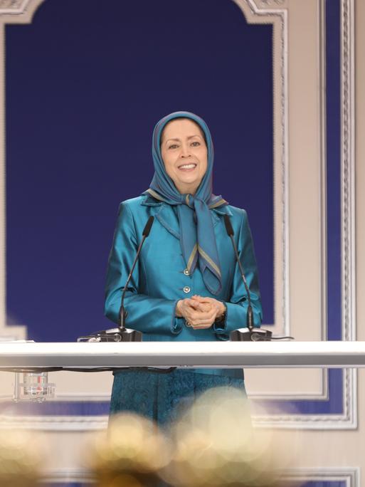 Die Parteivorsitzende der Volksmudschahedin Maryam Rajavi bei einer Rede. Sie trägt ein türkisenes Kostüm und ein türkisfarbenes Kopftuch.
