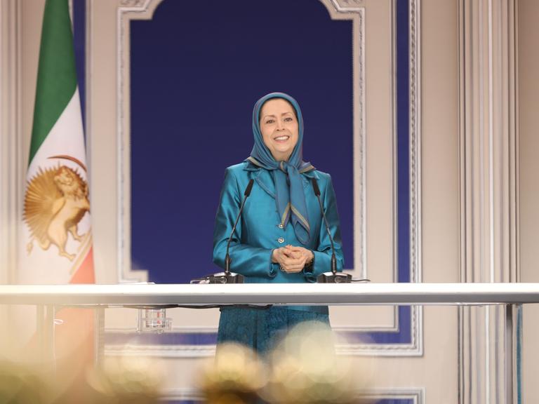 Die Parteivorsitzende der Volksmudschahedin Maryam Rajavi bei einer Rede. Sie trägt ein türkisenes Kostüm und ein türkisfarbenes Kopftuch.