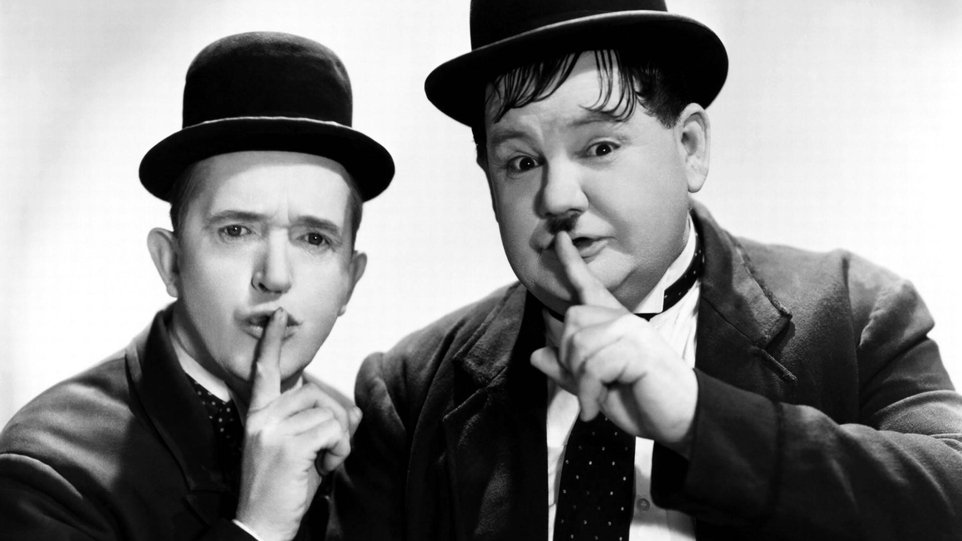 Stan Laurel und Oliver Hardy halten ihre Finger an den Mund als Zeichen für das Schweigen.