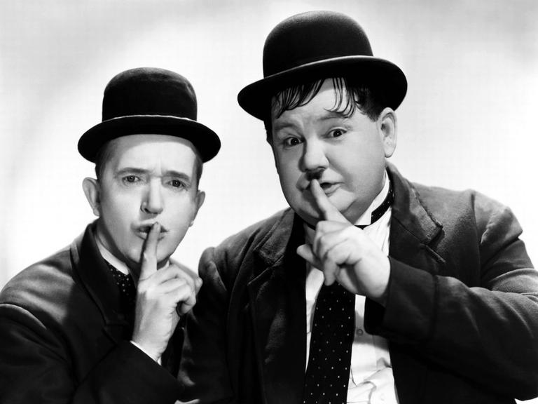 Stan Laurel und Oliver Hardy halten ihre Finger an den Mund als Zeichen für das Schweigen.