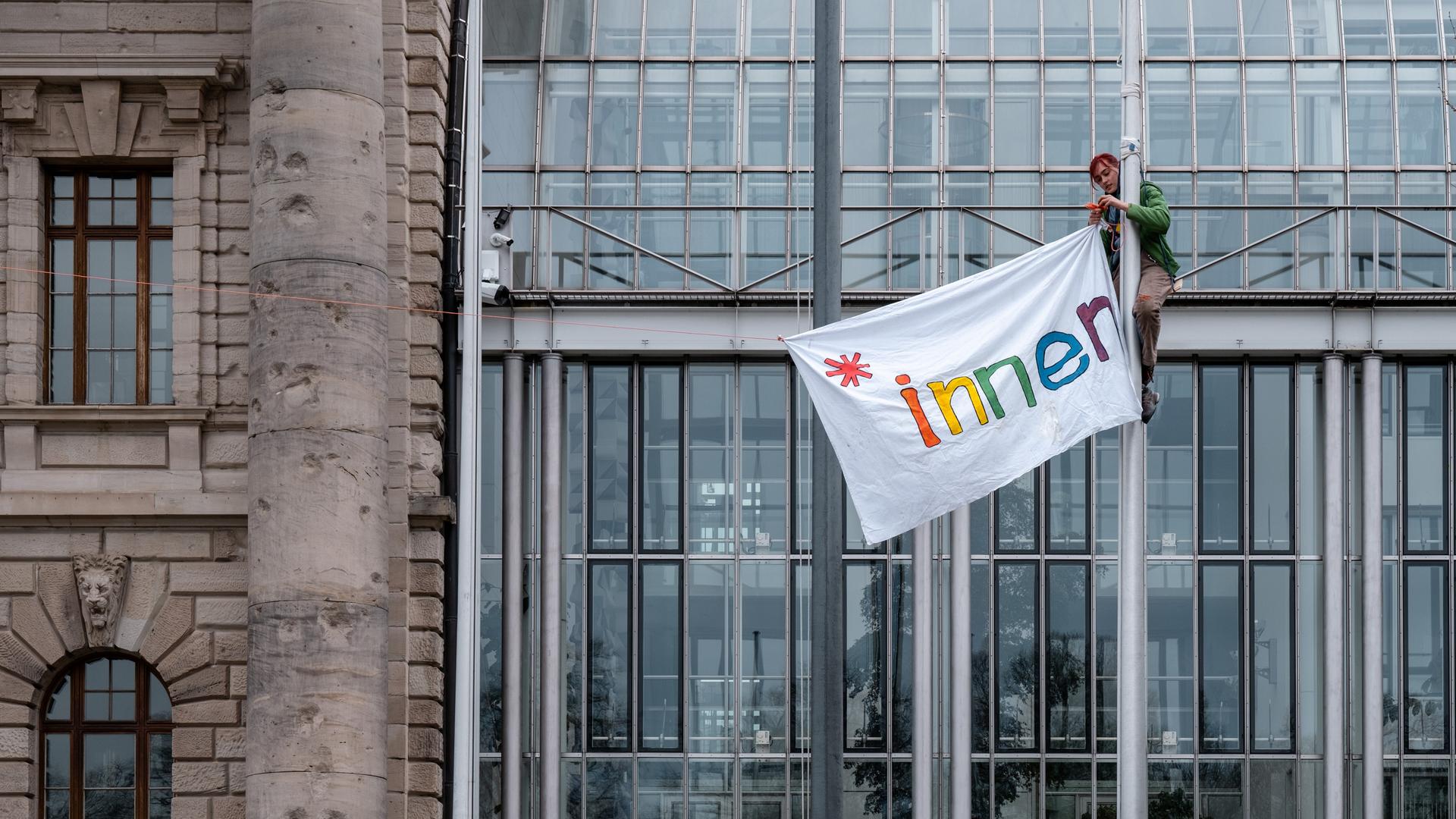 Vor der Bayerischen Staatskanzlei in München hissen Protestierende an Fahnenmasten ein Banner mit der Aufschift "*innen".