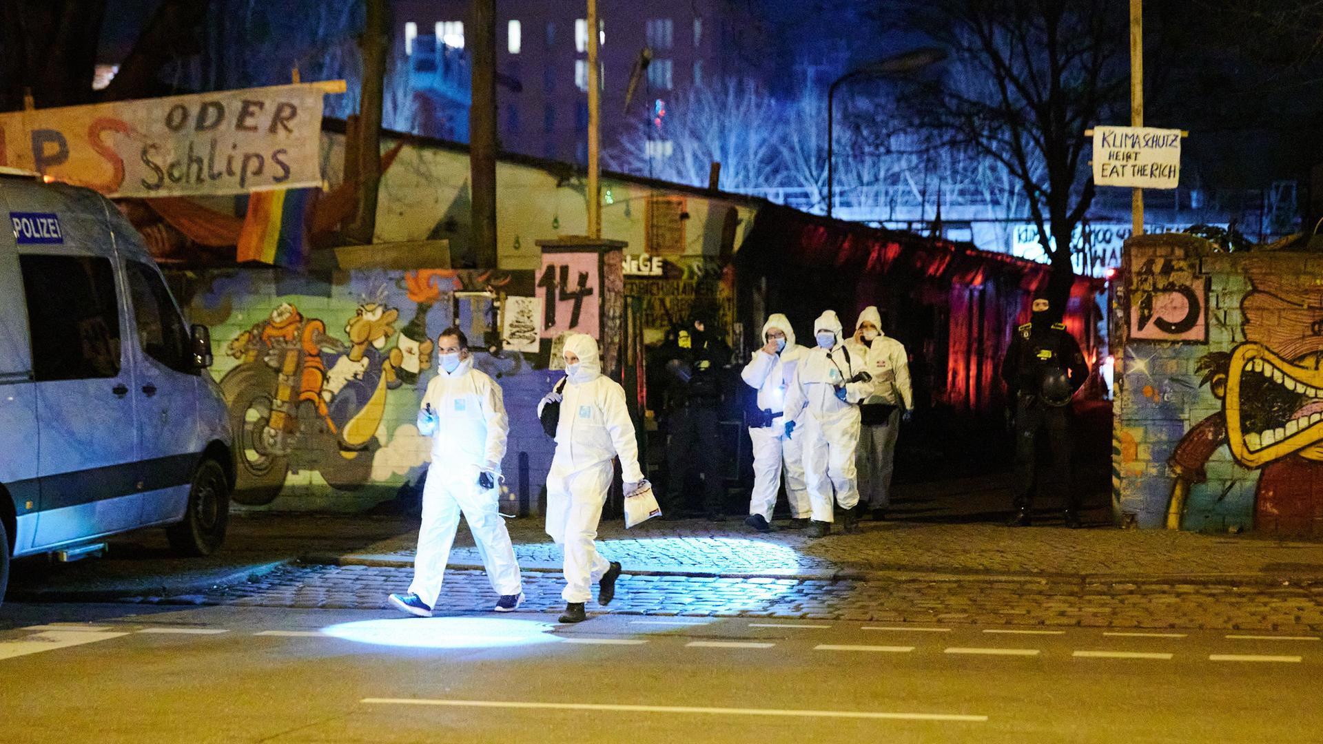 Berlin: Einsatzkräfte der Spurensicherung in weißen Schutzanzügen kommen von dem Bauwagengelände zurück.