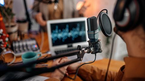 Zwei Personen sitzen in einem Studio vor Mikrofonen und Laptops.