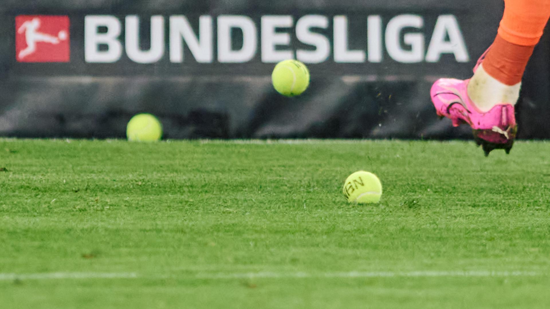Dortmunds Torwart Gregor Kobel schießt Tennisbälle vom Platz, die Fans aus Protest gegen Investoren in der DFL auf das Spielfeld geworfen haben.