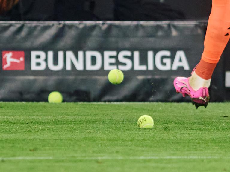 Dortmunds Torwart Gregor Kobel schießt Tennisbälle vom Platz, die Fans aus Protest gegen Investoren in der DFL auf das Spielfeld geworfen haben.