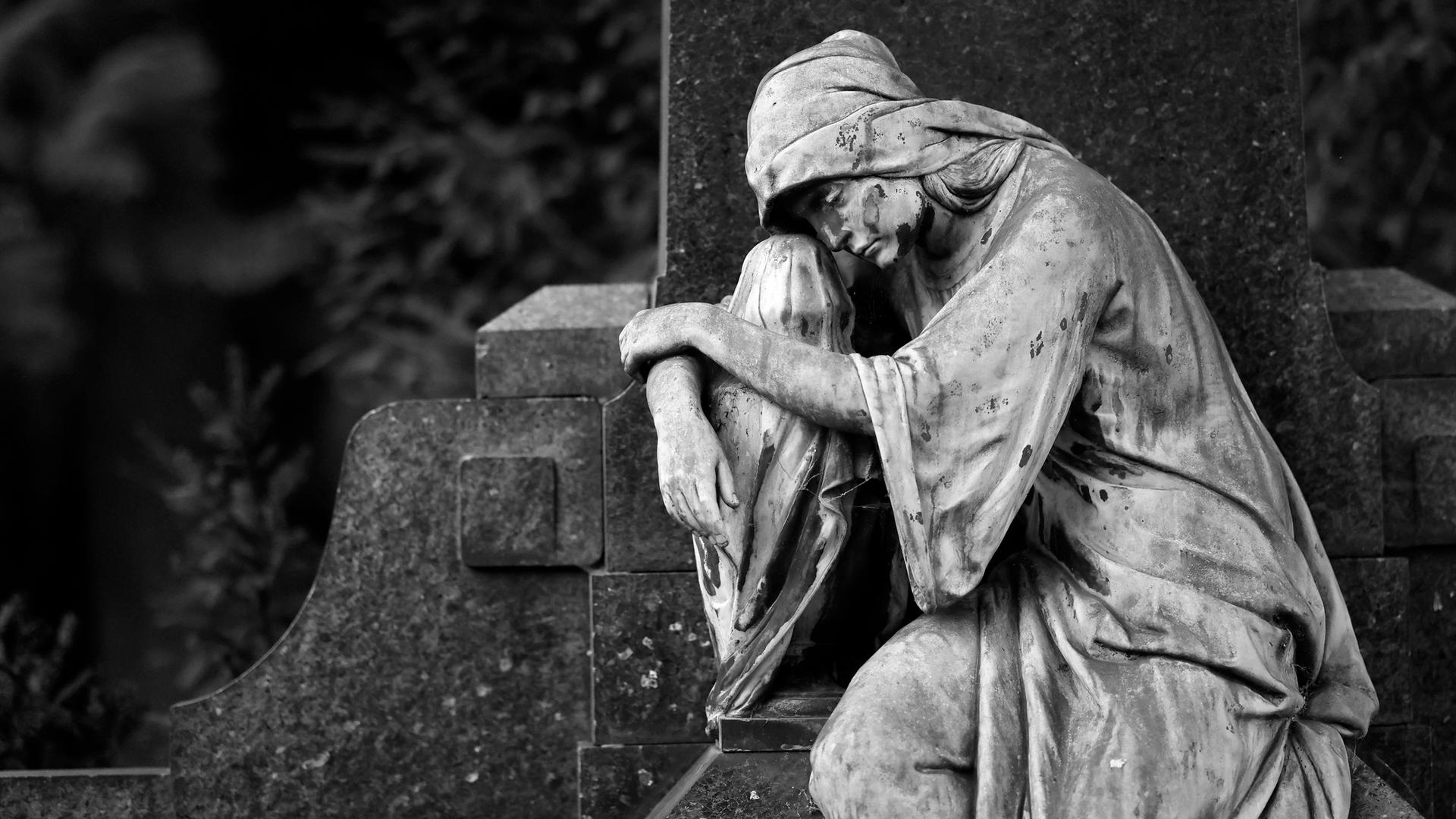 Eine trauernde Grabfigur aus Stein auf dem Melaten-Friedhof in Köln.