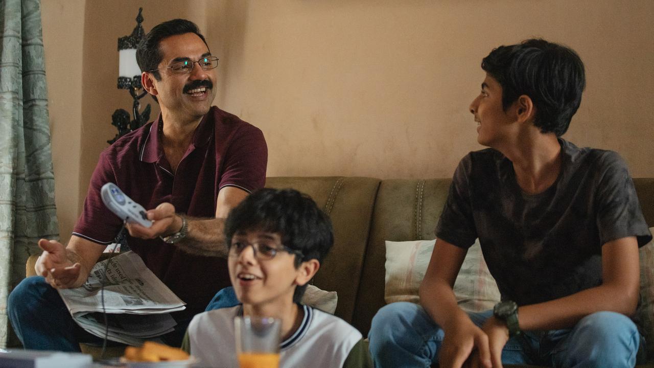 Filmszene aus der Serie "Trial by Fire". Zu sehen ist ein lachender Vater mit seinen Söhne auf einer Couch in einer Art Wohnzimmer. Der Vater hält in seiner Hand einen Controller einer Videokonsole.