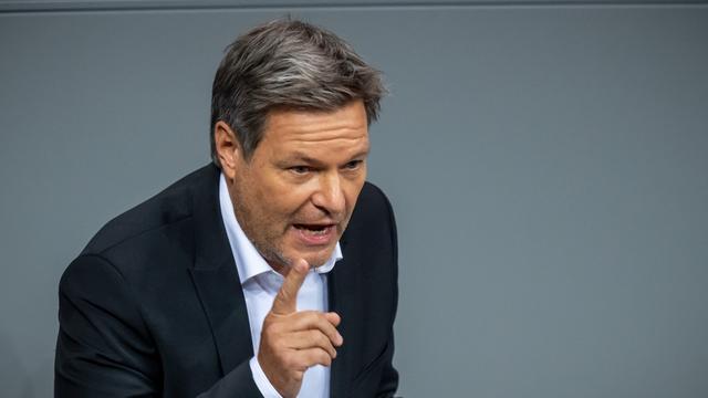 Robert Habeck, Bundesminister für Wirtschaft und Klimaschutz, spricht und erhebt den Zeigefinger der rechten Hand. Er trägt einen Anzug und steht vor einer grauen Wand.