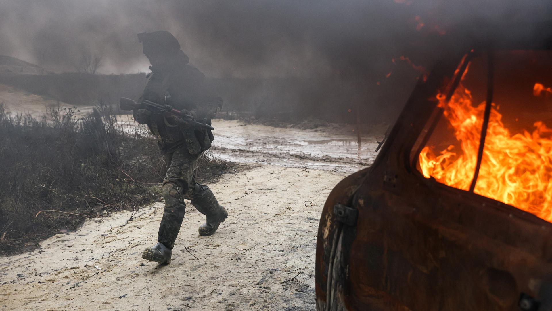 Ein Soldat mit einem Gewehr geht an einem brennenden Auto in der Region Lugansk vorbei. Ein Soldat mit einem Gewehr geht an einem brennenden Auto in der Region Lugansk vorbei.