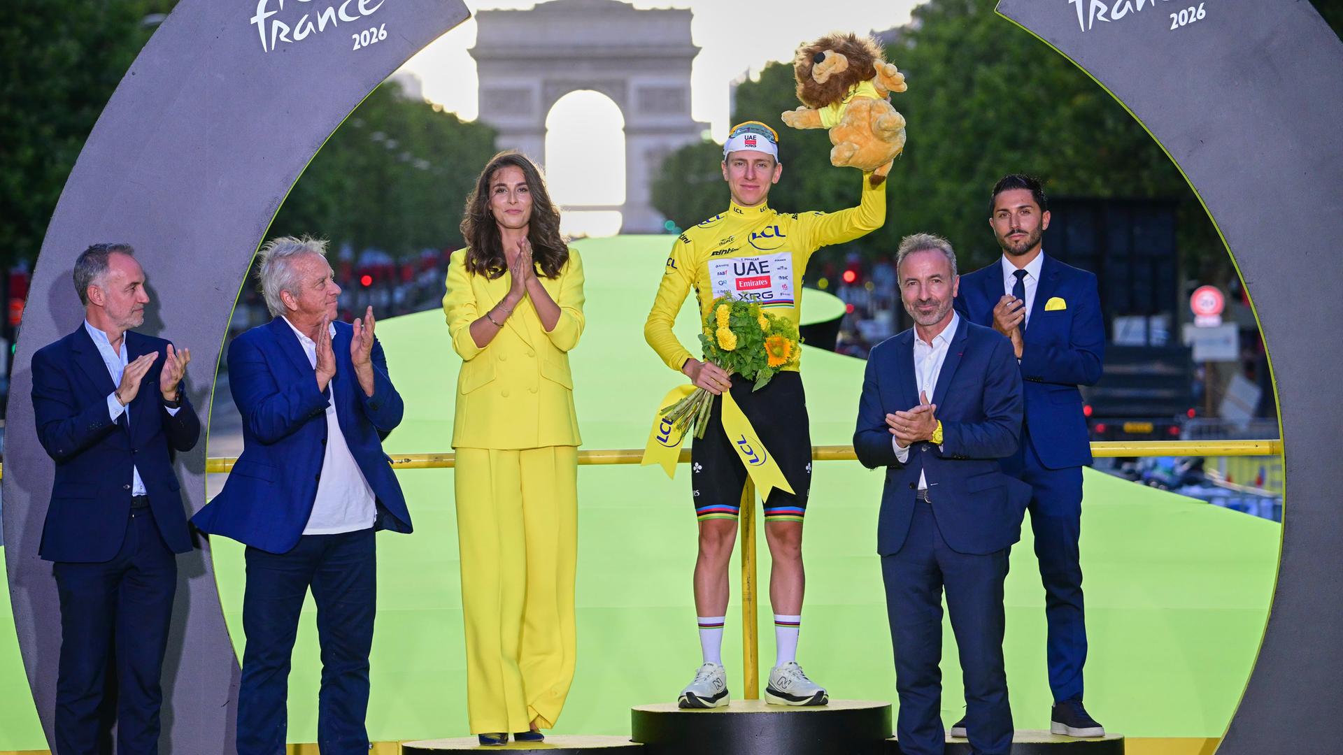 Siegerehrung bei der Tour de France - Gewinner Tadej Pogacar steht auf Siegertreppchen und hält Blumenstrauß hoch Siegerehrung bei der Tour de France - Gewinner Tadej Pogacar steht auf Siegertreppchen und hält Blumenstrauß hoch