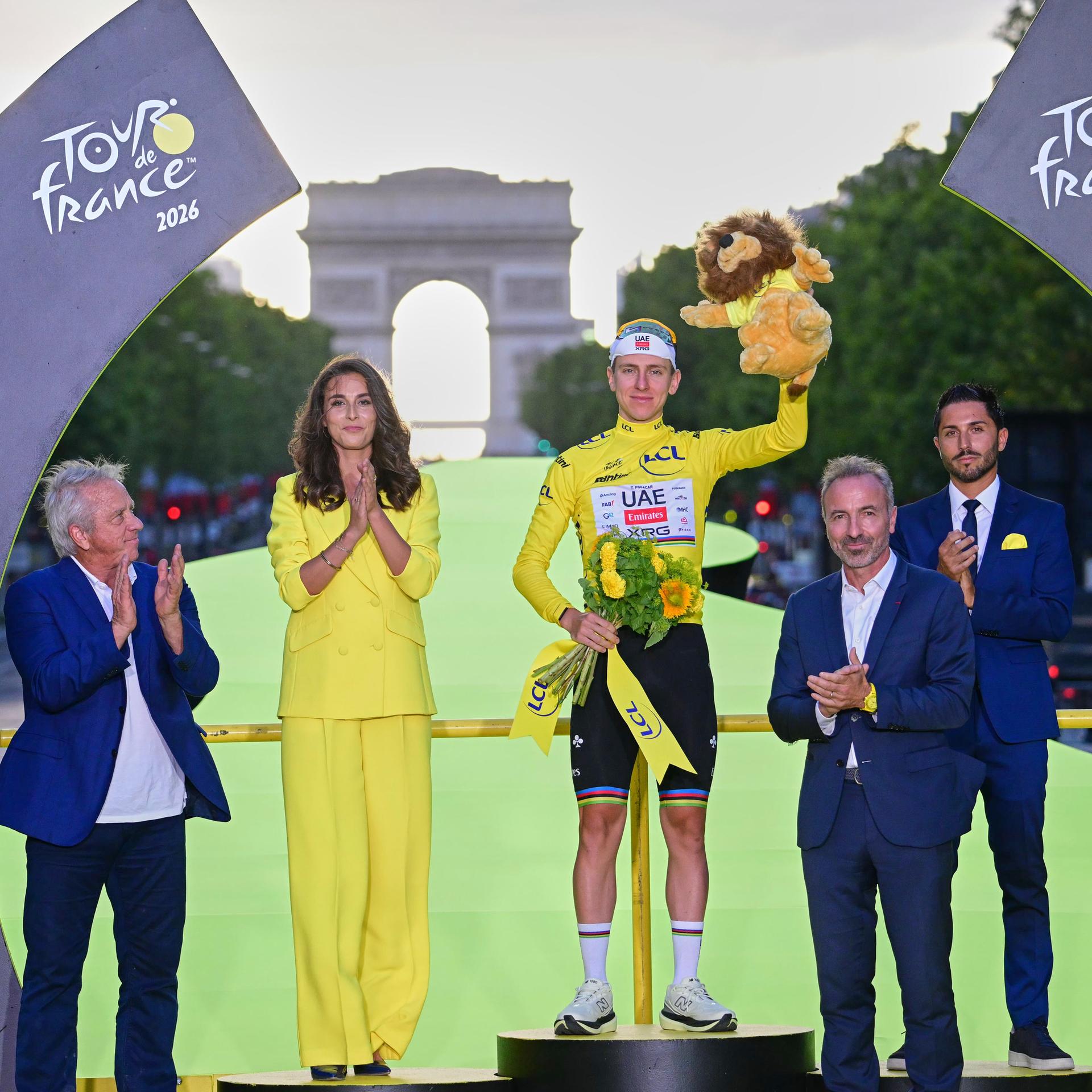 Siegerehrung bei der Tour de France - Gewinner Tadej Pogacar steht auf Siegertreppchen und hält Blumenstrauß hoch