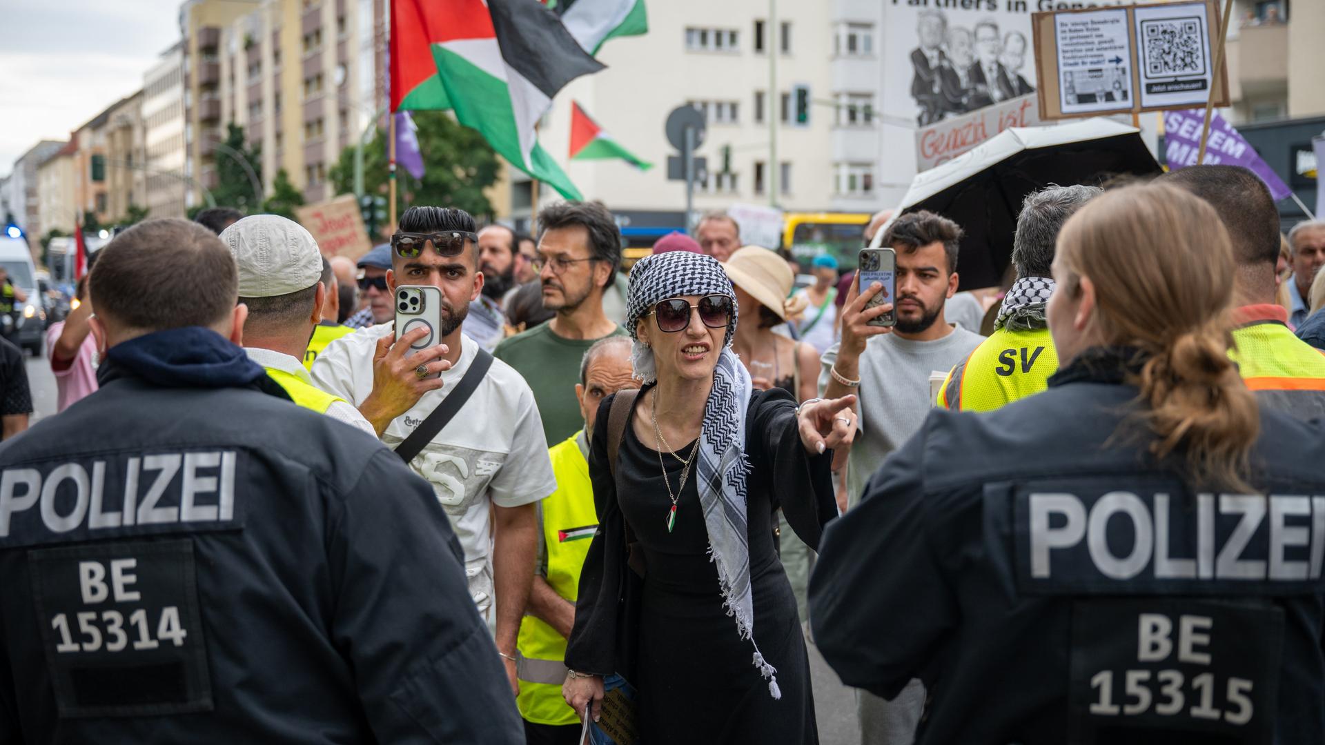 Protestierende und Polizisten stehen sich auf einer Straße gegenüber. Im Hintergrund sind palästinensische Flaggen zu sehen.