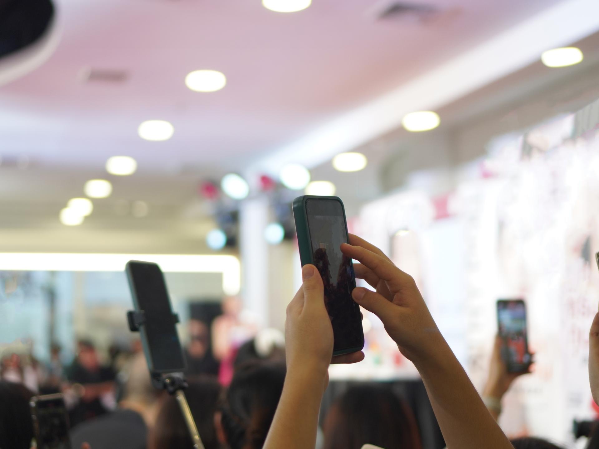 Mehrere Personen filmen eine Veranstaltung im Hintergrund mit ihren Smartphones im Hochformat.