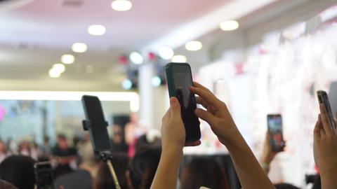 Mehrere Personen filmen eine Veranstaltung im Hintergrund mit ihren Smartphones im Hochformat.