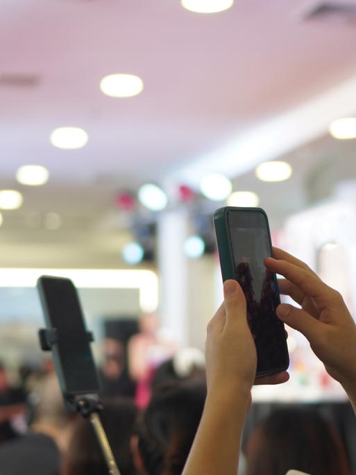 Mehrere Personen filmen eine Veranstaltung im Hintergrund mit ihren Smartphones im Hochformat.