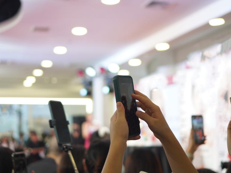 Mehrere Personen filmen eine Veranstaltung im Hintergrund mit ihren Smartphones im Hochformat.