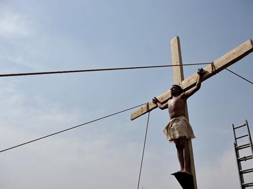 Ein Darsteller steht an einem Holzkreuz und imitiert die Kreuzigung Jesu. Im Hintergrund blauer Himmel.