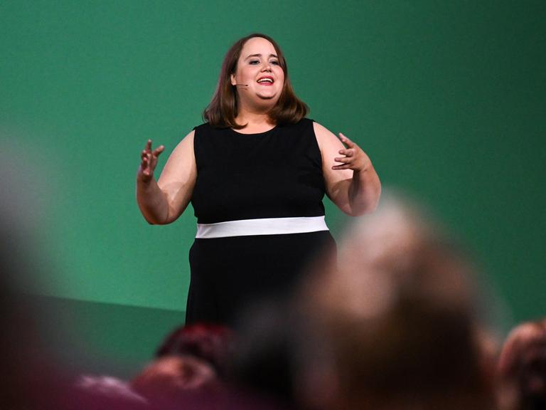 Ricarda Lang steht im schwarzen Kleid auf einer Bühne und spricht zu Publikum.