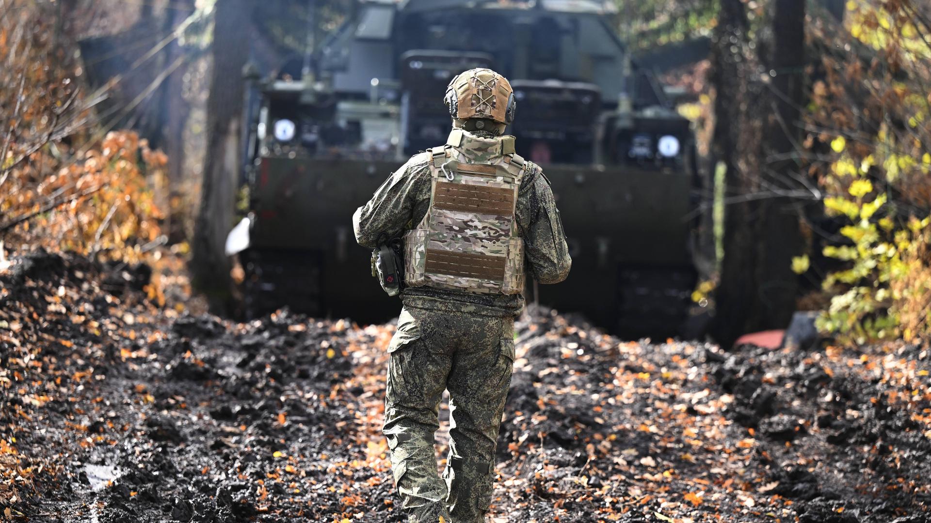 Ein Soldat geht mit dem Rücken zur Kamera auf einen Panzer zu. Er trägt eine kugelsichere Weste und einen Schutzhelm. Ein Soldat geht mit dem Rücken zur Kamera auf einen Panzer zu. Er trägt eine kugelsichere Weste und einen Schutzhelm.