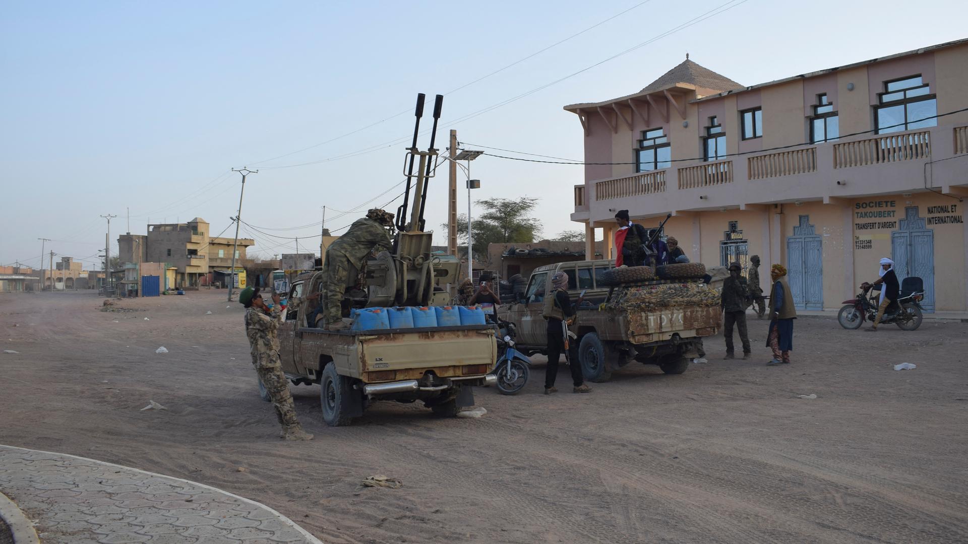Mehrere bewaffnete Personen befinden sich auf der Ladefläche von zwei Pickups.