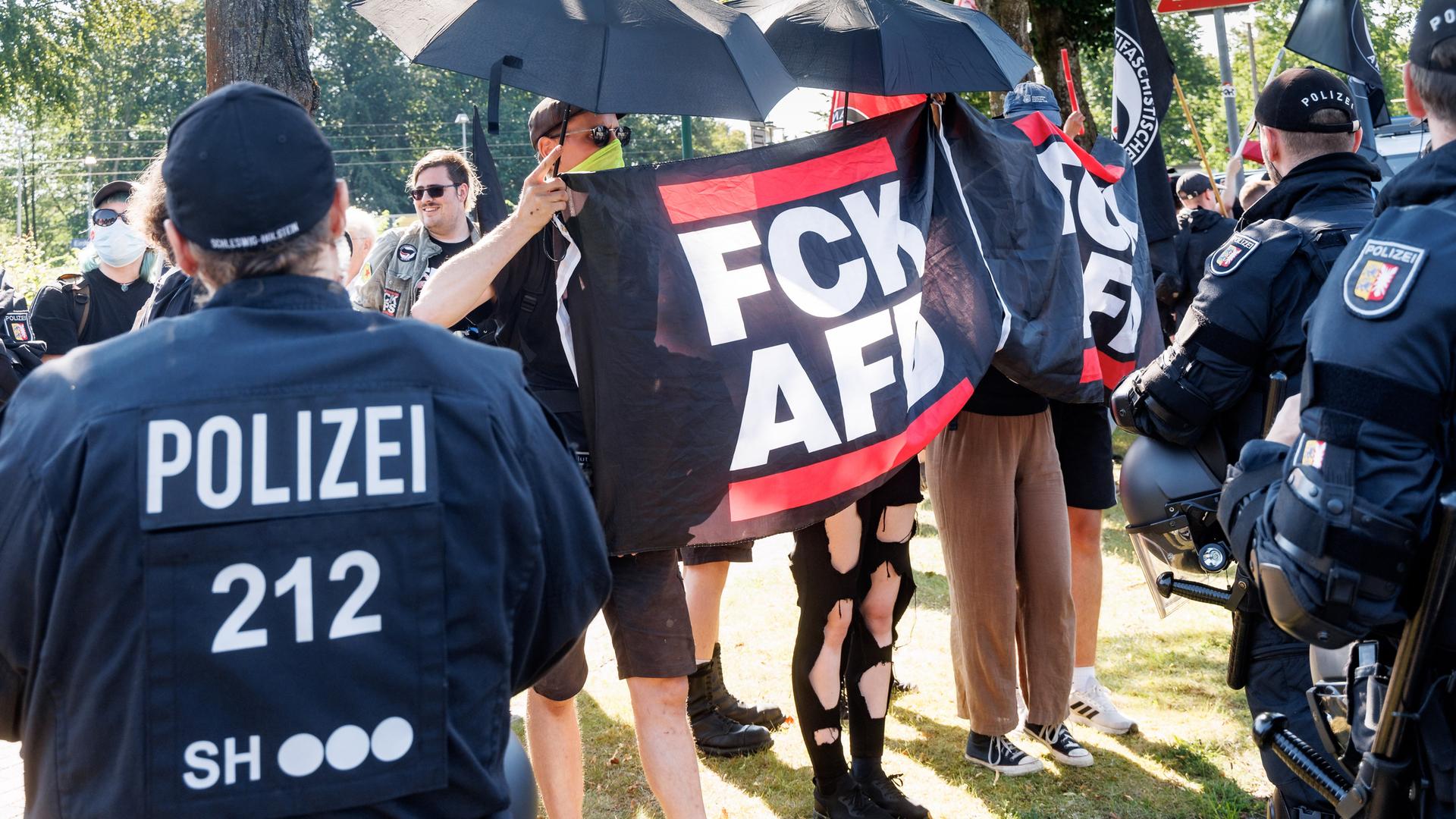 Demonstranten protestieren gegen ein von der AfD organisiertes Treffen in Neumünster. Sie halten Plakate mit der Aufschrift "FCK AFD" und sind von Polizisten umgeben. 