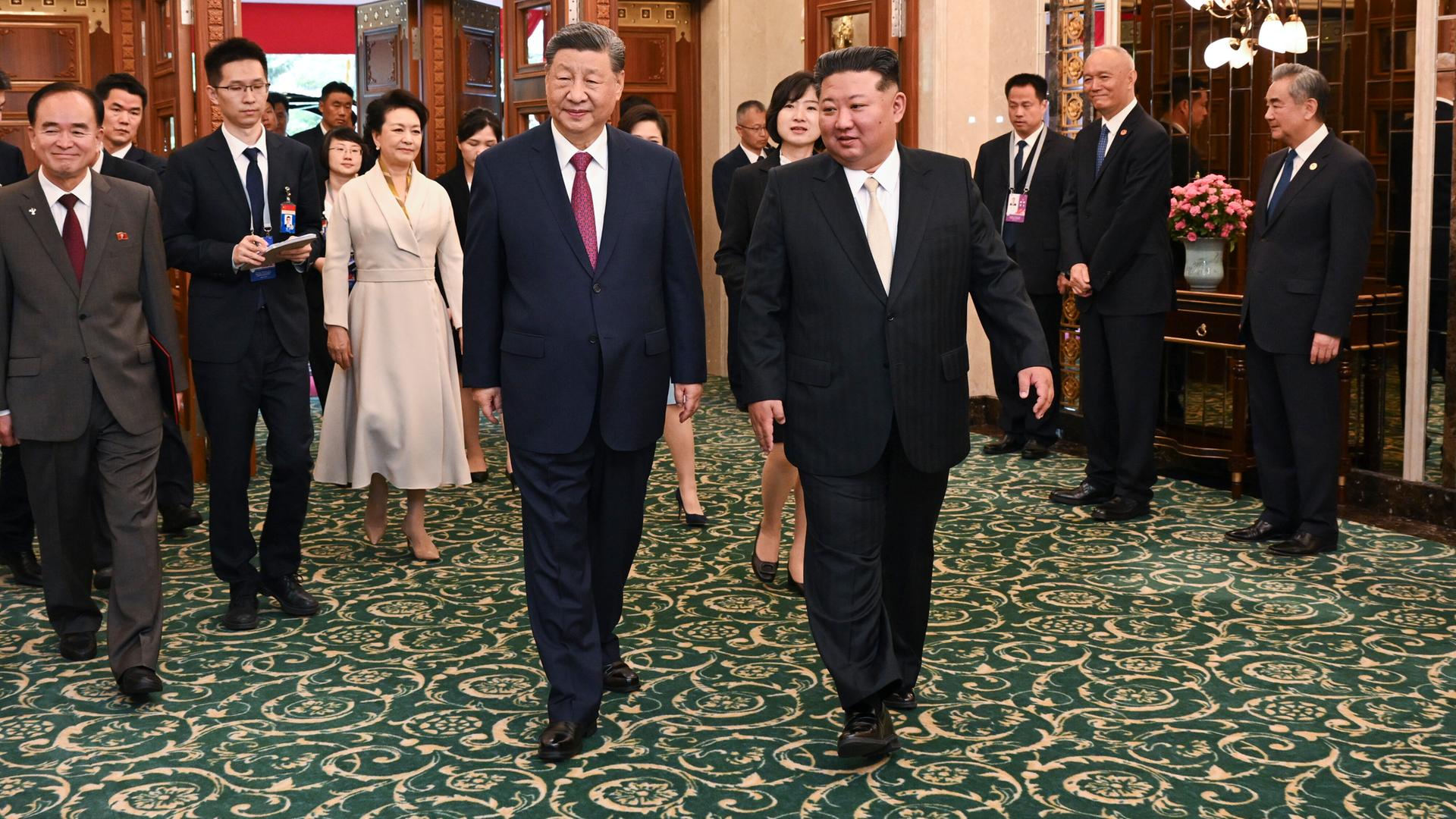 Der nordkoreanische Staatschef Kim Jong Un (l) und der chinesische Präsident Xi Jinping (r) kommen mit Begleitung aus einem Raum.