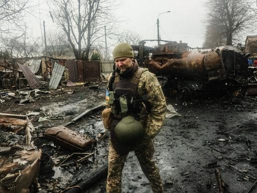 Ein ukrainischer Soldat läuft durch eine kriegsverwüstete Straße. Er inspiziert die Trümmer eines russischen Panzers.